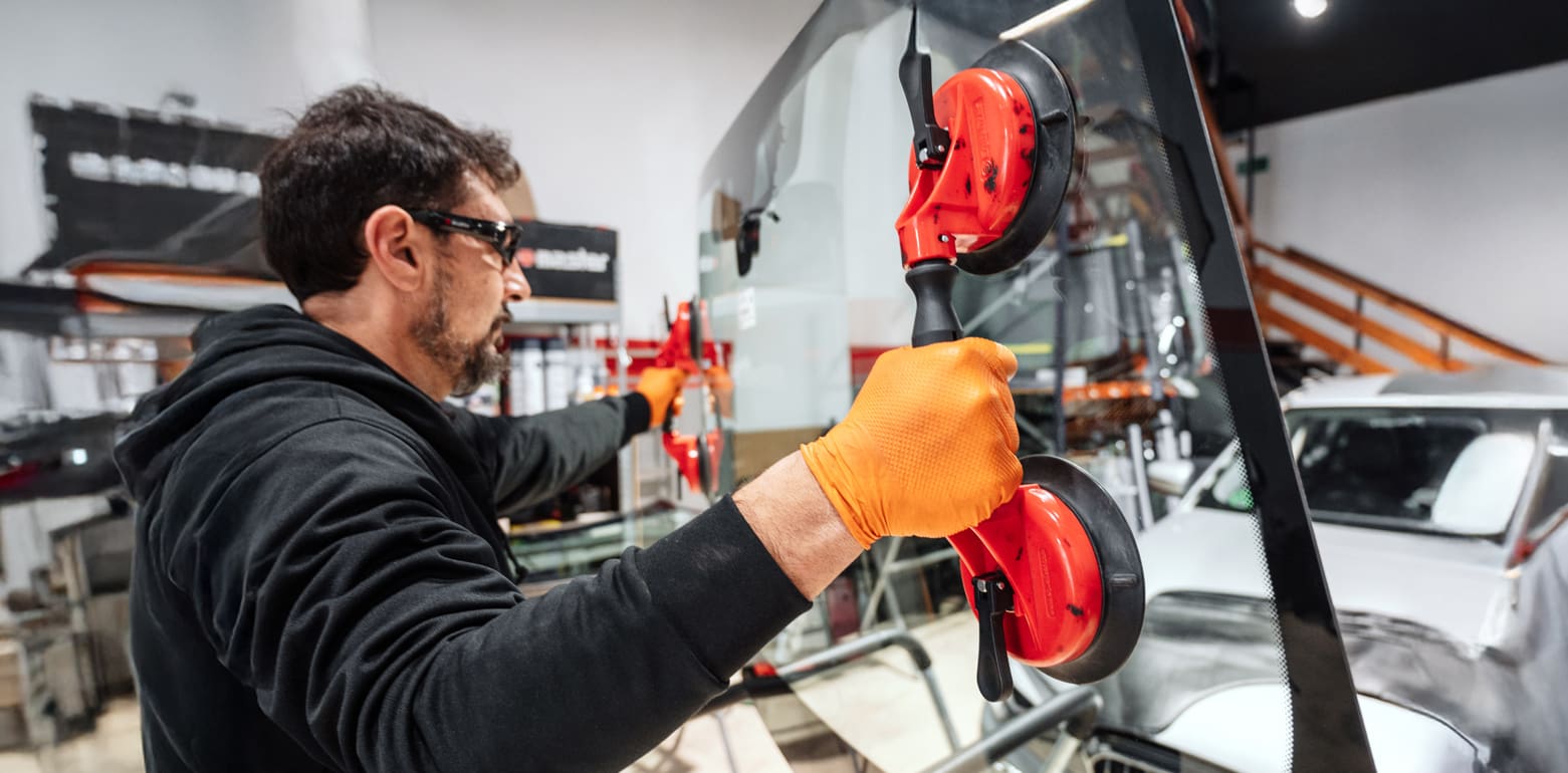 Automobile technician worker replacing windscreen or windshield of a car in auto service station garage.